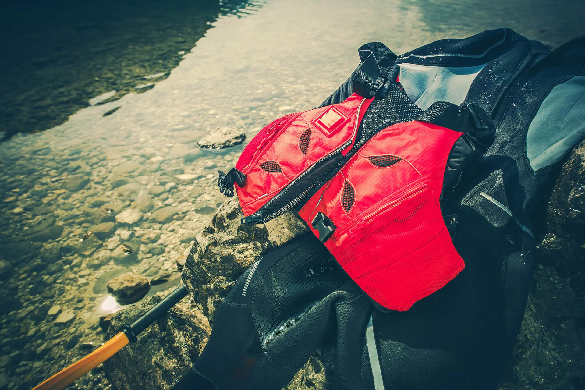 Wetsuit, life vest and paddle on the rocks by the river